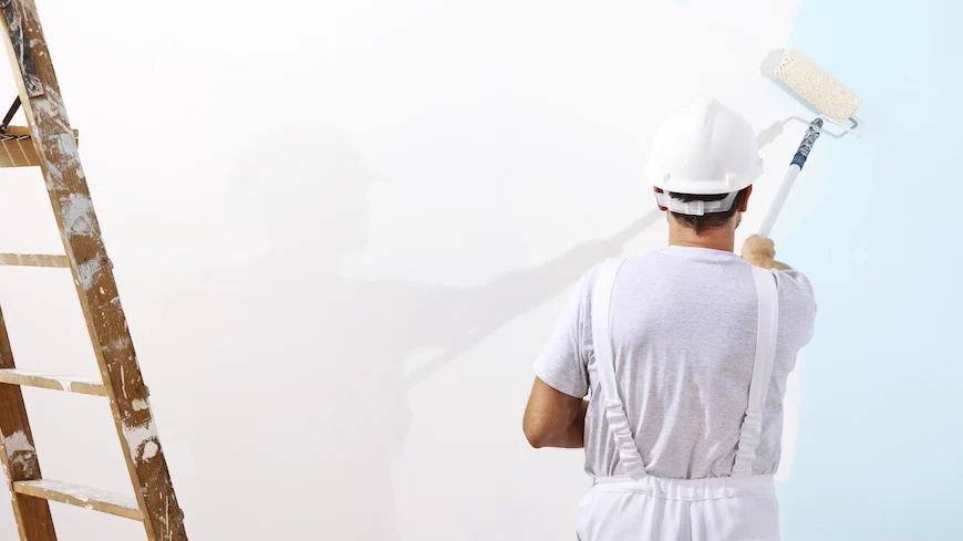 Professional painter with a paint roller making a white wall a light shade of blue