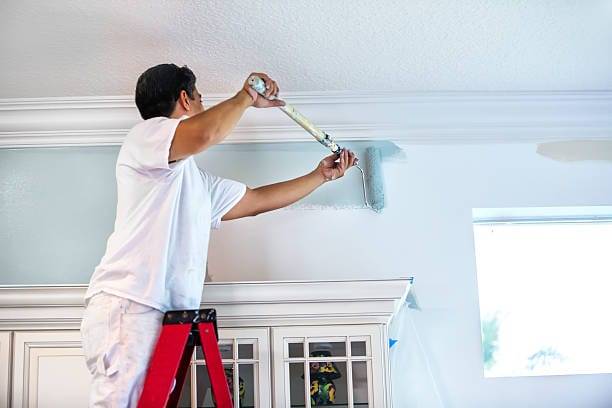 A housepainter stands on a ladder to paint the walls inside a residential home